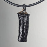 Black textured pendant shaped like a small horn or tusk, hanging from a black braided cord against a neutral background.