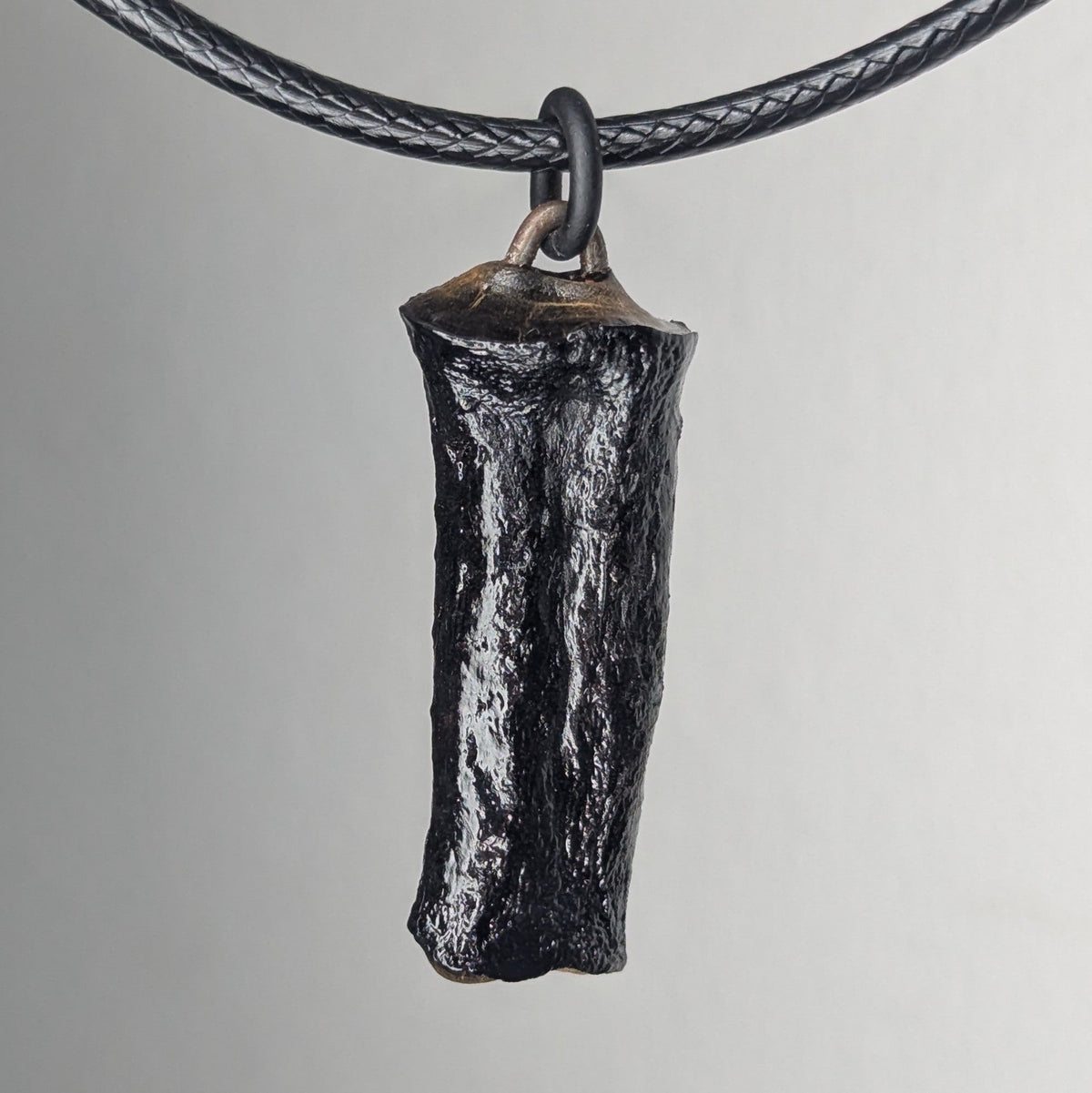Black textured pendant shaped like a small horn or tusk, hanging from a black braided cord against a neutral background.