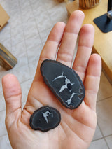 Hand holding two black thunder egg slices with gray and white intricate star-shaped patterns inside, shown against a tiled floor background.