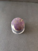 Rounded purpurite stone with deep purple and lighter beige veins, placed on a clear circular stand against a dark gray background.