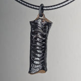 Glossy black pendant with raised rib-like texture hanging from a black braided cord against a neutral background.