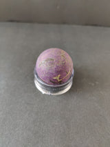 Polished purple purpurite sphere with gold mineral veins, displayed on a small clear round stand against a gray background.