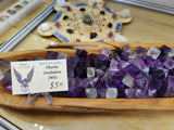 Cluster of medium-sized fluorite octahedrons in purple and translucent hues displayed in a wooden tray, with a handwritten price tag of $5.00 nearby.