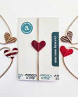 Five macrame bracelets with heart-shaped patterns in shades of red, beige, and brown, one displayed on a card labeled ‘macrame bracelet’ and ‘adjustable handmade’.
