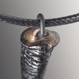 Close-up of a pendant with a textured black surface and metallic highlights, suspended on a braided black cord through a circular loop.