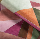 Close-up of a pillow cover fabric with an abstract geometric pattern featuring irregular shapes in shades of rose, orange, green, brown, and pink with thin white outlines.