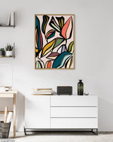 Abstract framed canvas featuring colorful overlapping leaf shapes in teal, coral, mustard, and black outlines, hanging above a white modern dresser in a minimal room.