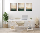 Three framed abstract canvas artworks with layered green and beige hues above a white desk, accompanied by beige chair, potted plants, and light wood flooring.