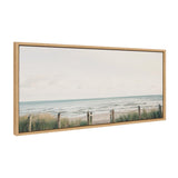 Framed canvas depicting a serene beach scene with sandy dunes, green grasses, a rope fence, and a cloudy pale sky above calm ocean waves.