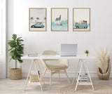 Minimalist white office with a white desk and beige chair, featuring three framed canvases above: vintage car with palm trees, zebra surfing, van loaded with luggage.