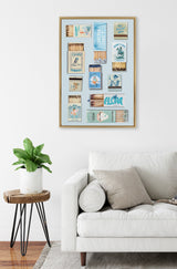 Gallery wall art print with vintage-style blue and tan matchbox illustrations arranged in a grid, framed in light wood above a white sofa and plant.