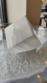 Polished translucent selenite cube standing on a wooden surface