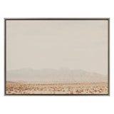Framed canvas print of a vast desert landscape with sparse shrubs and distant low mountains under a pale, overcast sky by Laura Evans.