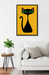 Framed minimalist illustration of a black cat with green eyes and pink ears on a bright mustard yellow background, hung above a white sofa in a modern living room.