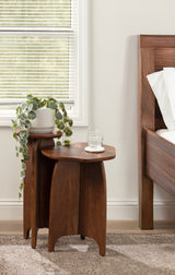 Two dark wood round tables with flared legs, one taller holding a potted trailing plant, the other shorter with a glass of water, placed beside a wooden bed frame.