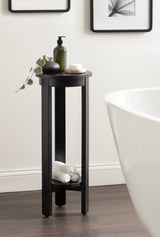 Tall, round black wood side table with an open lower shelf holding rolled white towels, placed beside a white bathtub on dark wooden floor.