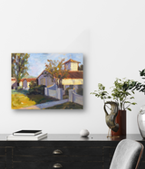 Oil painting of a sunlit villa with a tower, surrounded by a white fence and trees, displayed on a white wall above a black console with plants and books.