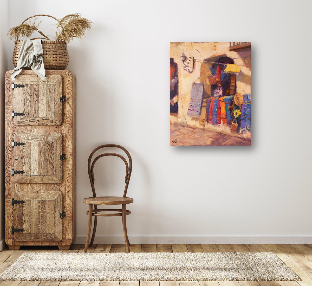Painting of vibrant sarapes hanging outside a sunlit building with colorful textiles and a sunflower detail, displayed on a plain white wall above a wooden chair.