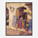 Oil painting of a sunlit stone wall with a small market stall displaying colorful woven sarapes and a straw hat beside a sunflower in a pot.