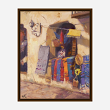 Oil painting of a sunlit rustic window displaying hanging sarapes in vibrant orange, blue, and red stripes alongside a sunflower in a pot and a straw hat.