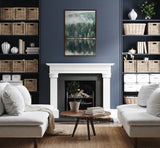 Cozy living room with white sofas facing each other, centered on a white fireplace with a framed forest reflection photo above, flanked by blue shelves with woven baskets.