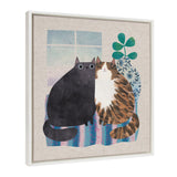 Framed canvas showing two stylized cats, one black and one brown tabby with white, sitting closely on a striped blue and purple rug in front of a window and leafy blue plant.
