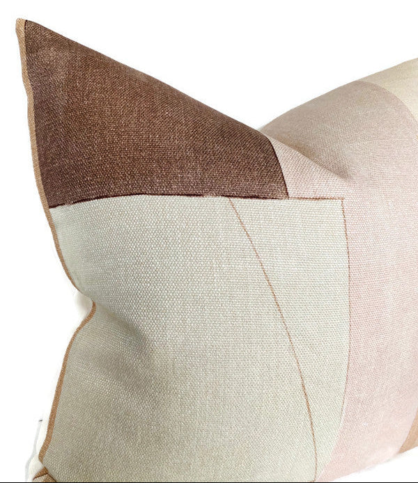 Close-up of a rectangular pillow cover in muted brown, beige, and soft pink geometric color blocks with visible textured weave and stitched seams.