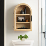 Light tan wooden wall cabinet with an arched top and two shelves, holding a black vase, a small amber jar, and a black-and-white framed photo, above a white toilet with a potted green plant.