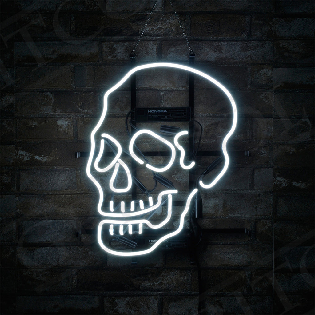 White neon light shaped like a human skull with prominent eye sockets and teeth, mounted on a dark brick wall with mounting hardware visible.