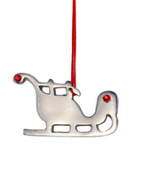 Silver metal sleigh Christmas ornament with cut-out windows and two small red gem accents hanging from a red string against a white background.