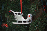 Set of four silver nickel finish sleigh Christmas tree ornaments each with red ruby crystals and red ribbons hanging on a holiday display.