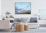 Framed canvas painting of a dramatic sky with clouds over a natural landscape, hung above a light gray sofa adorned with gray and navy cushions in a modern living room.