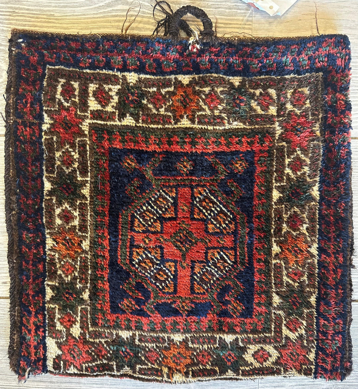 Small vintage Kurdish wool bag with a central red medallion and intricate geometric patterns in navy, cream, and earth tones, measuring about 14 inches square.