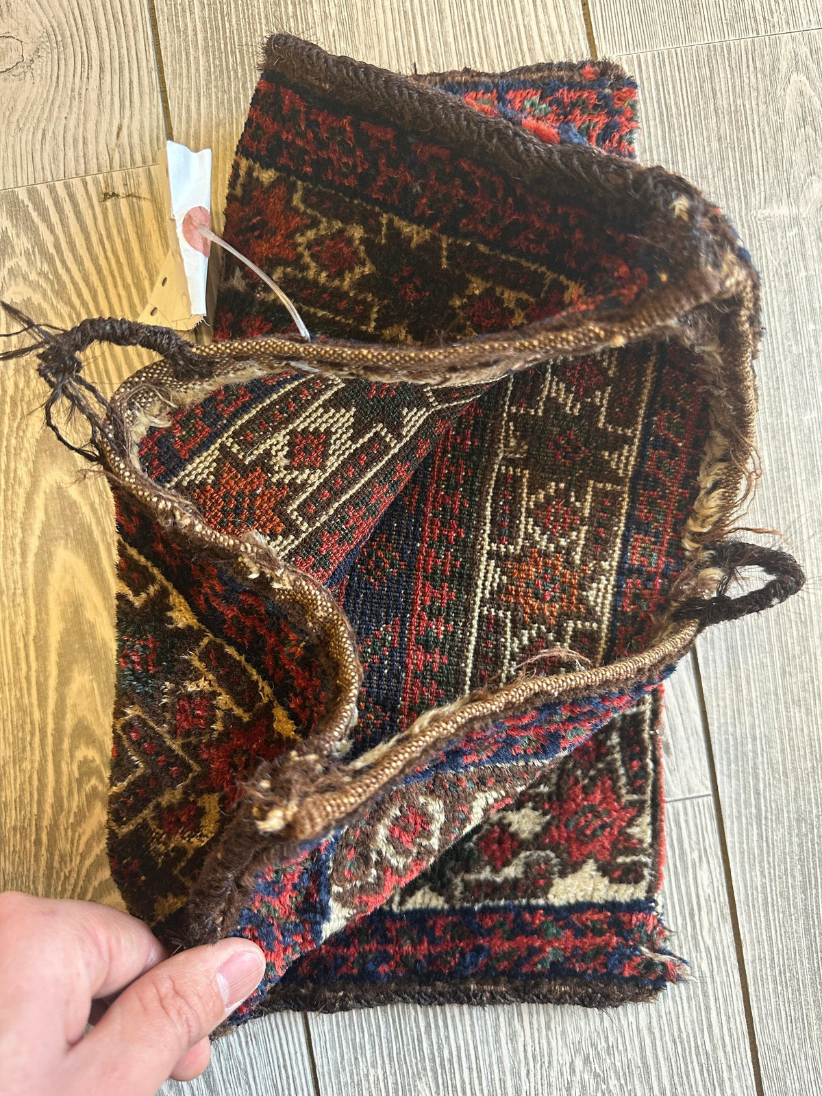 Small vintage Kurdish wool bag in rich reds, browns, and creams with geometric floral motifs, shown open with drawstring and textured fabric edges on a wooden floor.