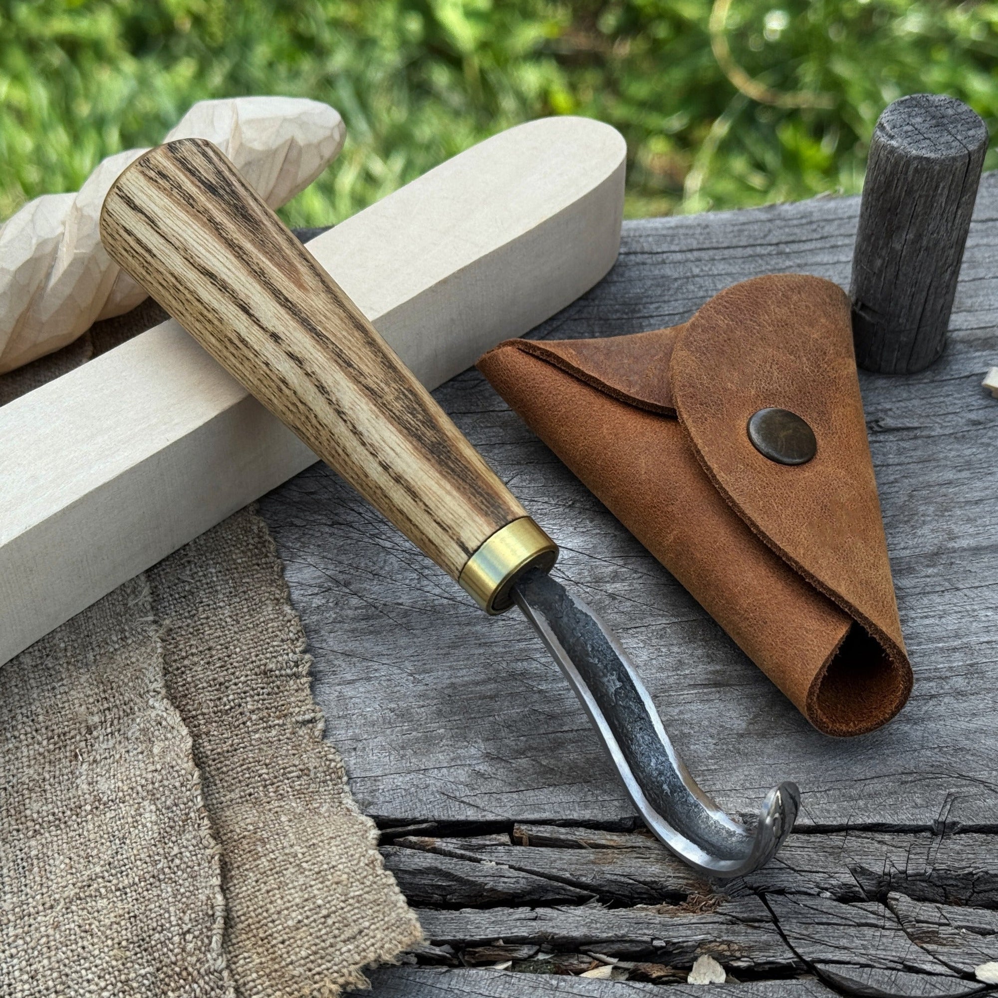 Spoon carving hook knife with curved blade and wooden handle, alongside leather sheath