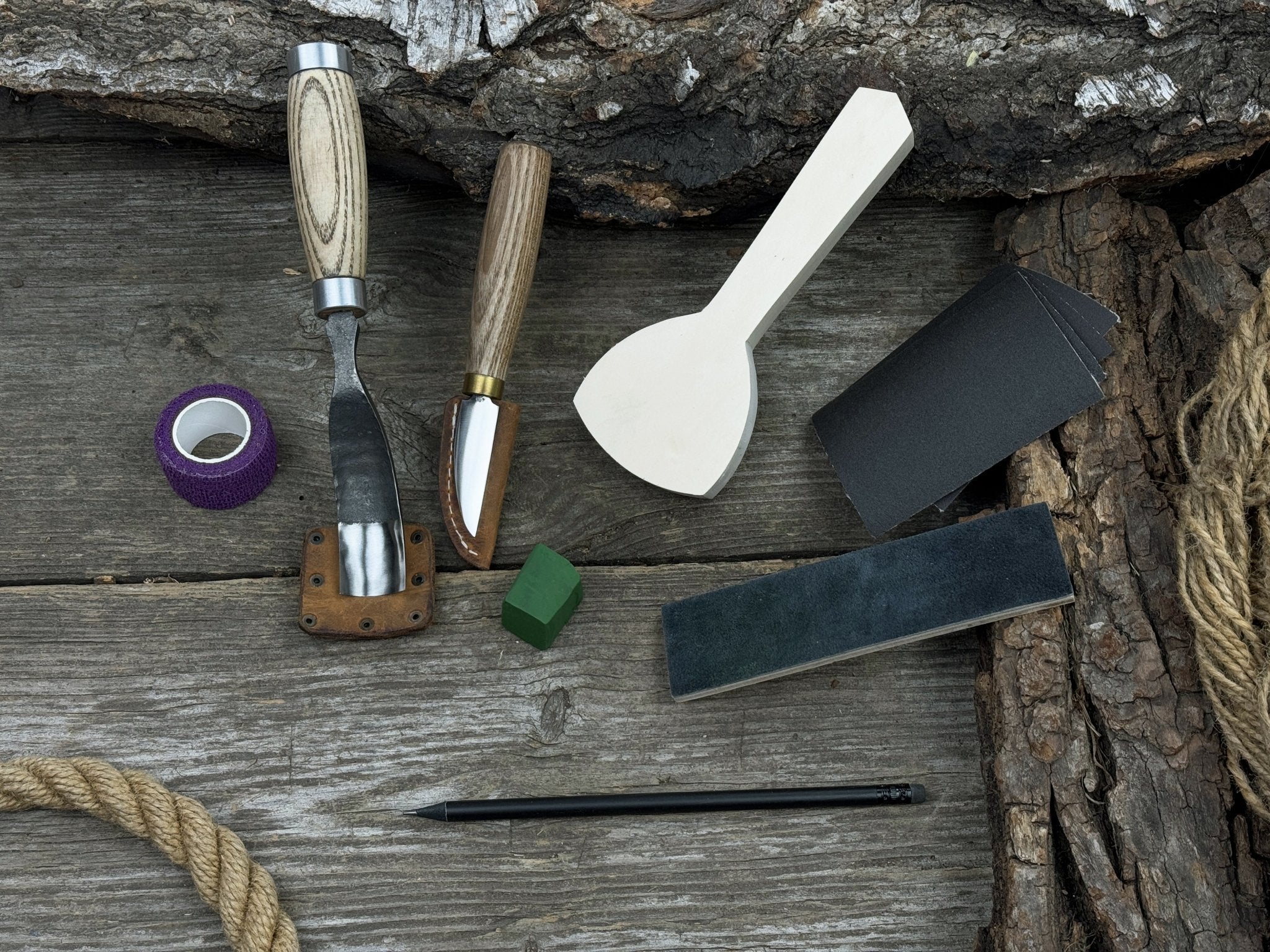 Spoon Carving Kit with bent gouge, whittling knife, wooden blank, sandpaper, sharpening board, pencil, and finger wrap