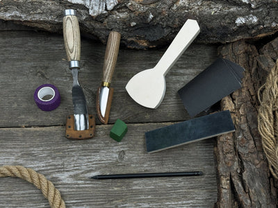 Spoon Carving Kit with bent gouge, whittling knife, wooden blank, sandpaper, sharpening board, pencil, and finger wrap