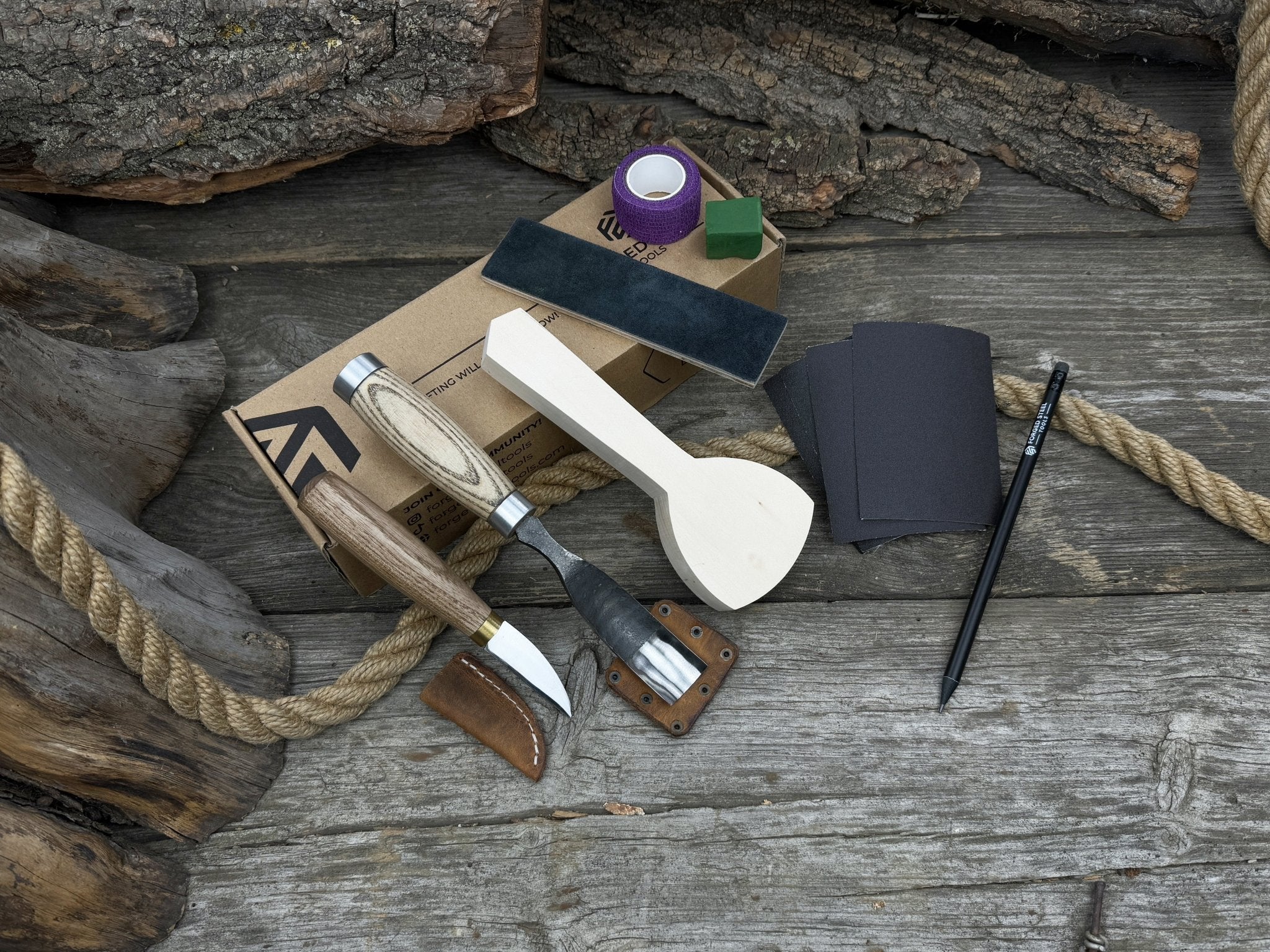 Spoon Carving Kit with bent gouge, whittling knife, wooden blank, sandpaper, sharpening board, pencil, and finger wrap