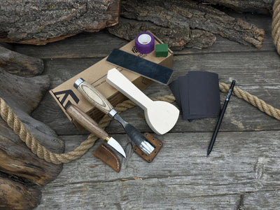 Spoon Carving Kit with bent gouge, whittling knife, wooden blank, sandpaper, sharpening board, pencil, and finger wrap