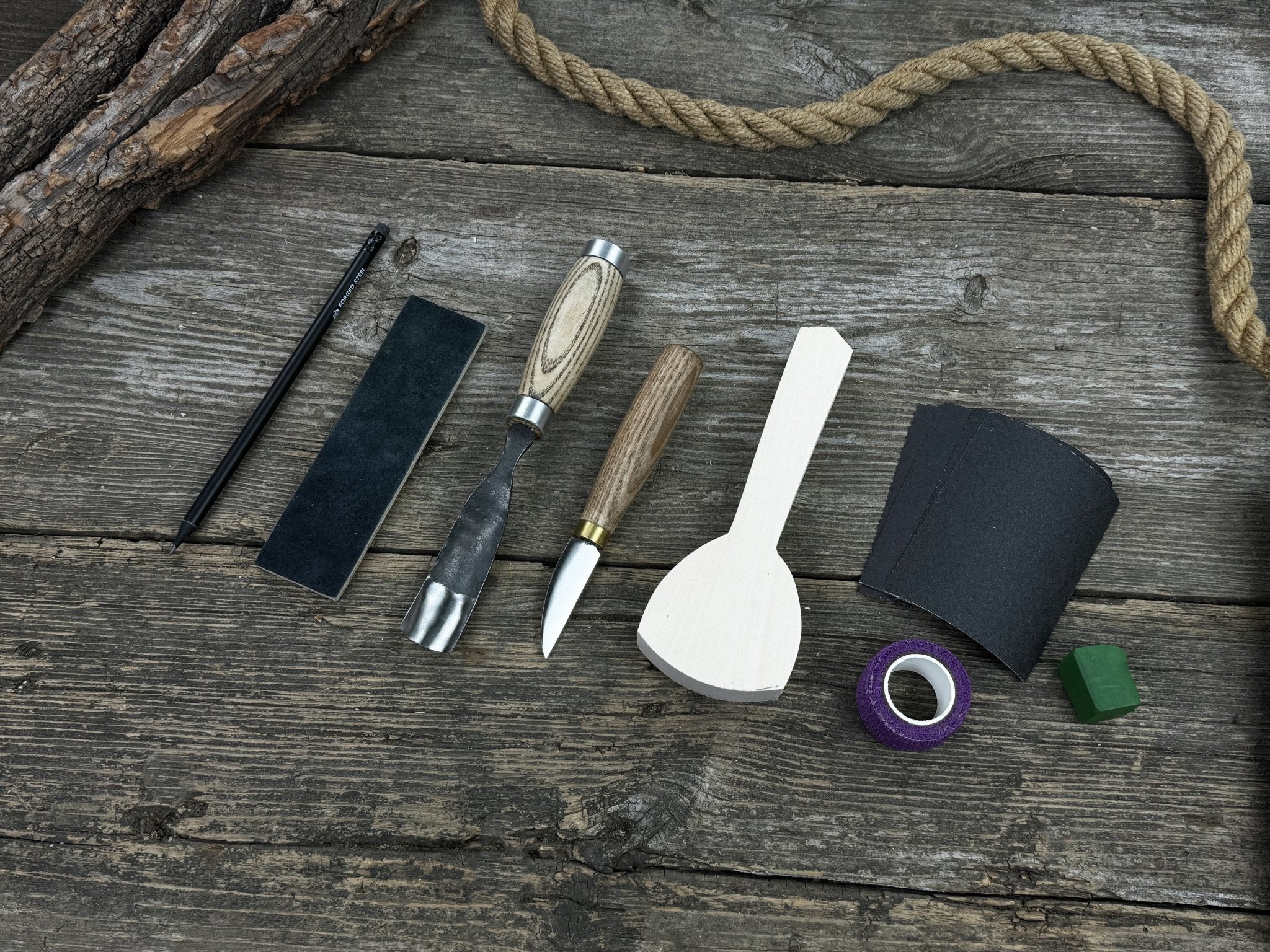 Spoon Carving Kit with bent gouge, whittling knife, wooden blank, sandpaper, sharpening board, pencil, and finger wrap