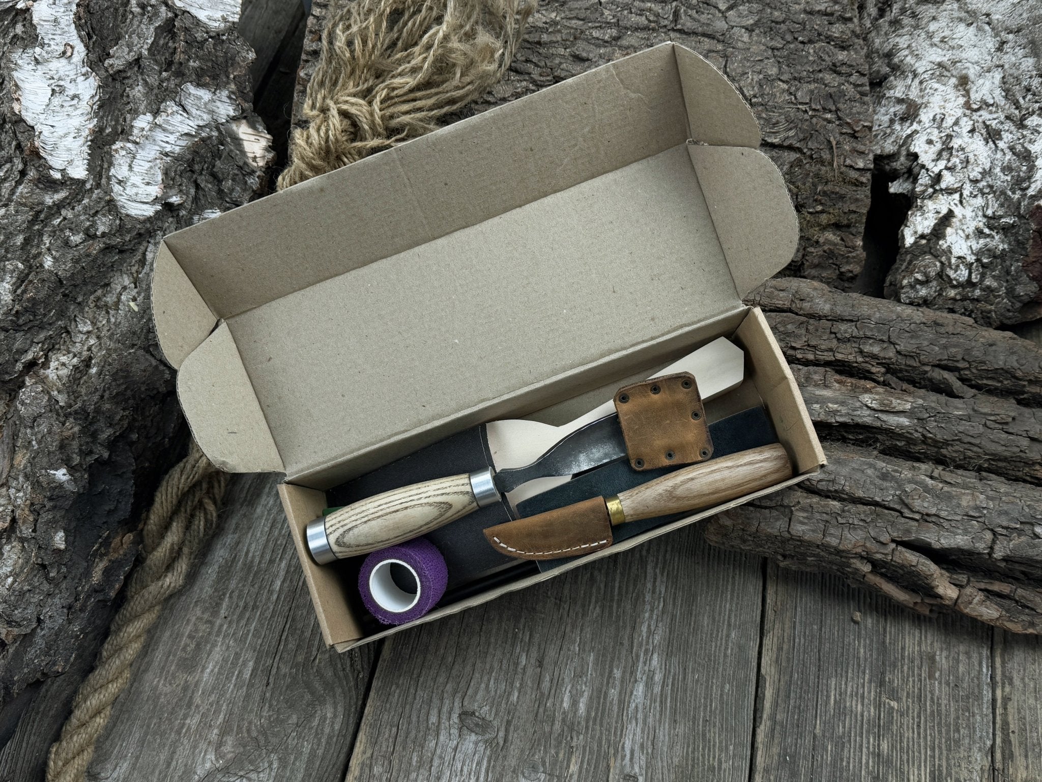 Spoon Carving Kit with bent gouge, whittling knife, wooden blank, sandpaper, sharpening board, pencil, and finger wrap