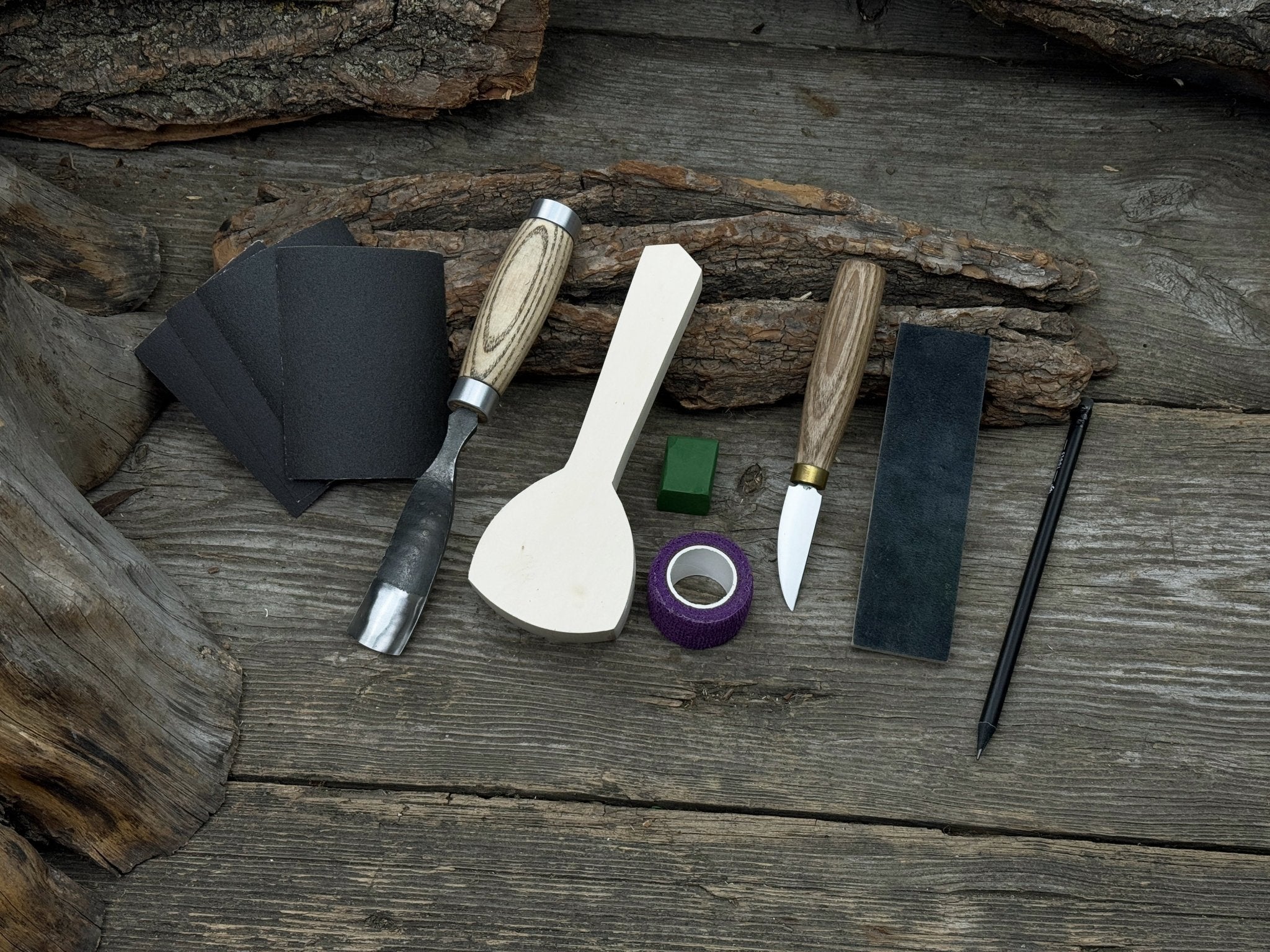 Spoon Carving Kit with bent gouge, whittling knife, wooden blank, sandpaper, sharpening board, pencil, and finger wrap