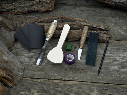 Spoon Carving Kit with bent gouge, whittling knife, wooden blank, sandpaper, sharpening board, pencil, and finger wrap