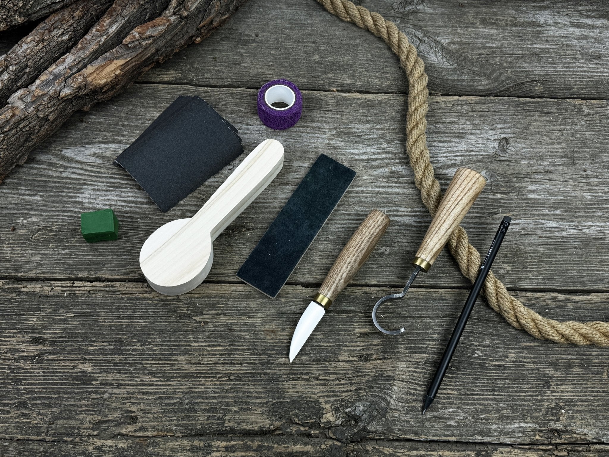 Spoon Carving Kit with knives, wooden blank, sandpaper, sharpening board, pencil, and finger wrap