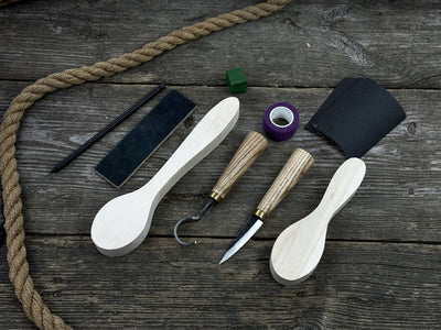 Complete spoon carving kit with knives, wooden blanks, sandpaper, sharpening board, pencil, and finger wrap
