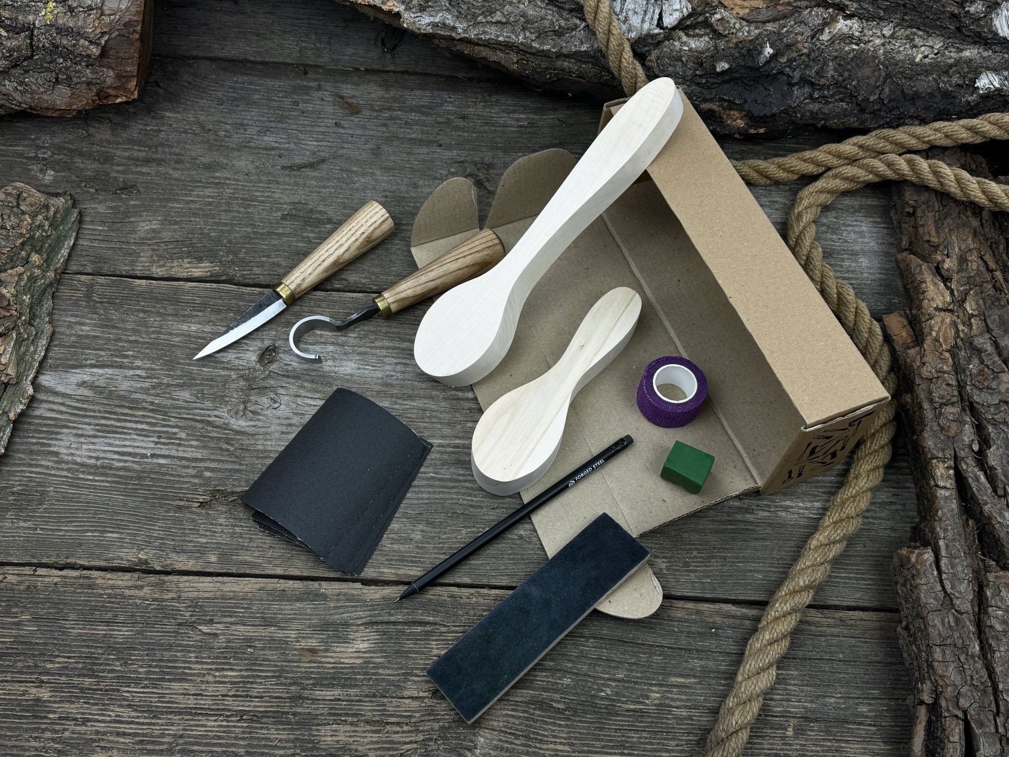 Complete spoon carving kit with knives, wooden blanks, sandpaper, sharpening board, pencil, and finger wrap