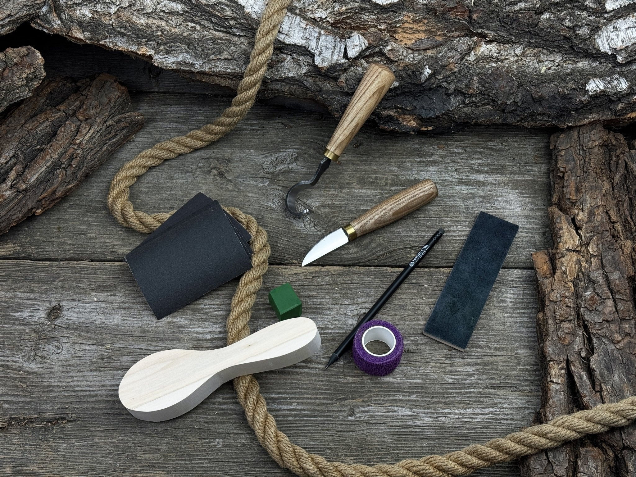 Spoon Carving Kit with knives, wooden blank, sandpaper, sharpening board, pencil, and finger wrap