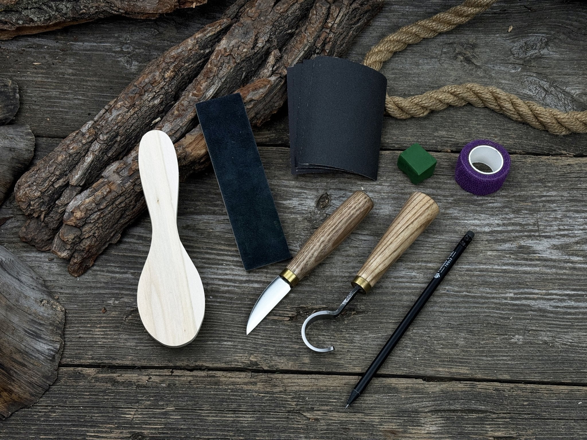 Spoon Carving Kit with knives, wooden blank, sandpaper, sharpening board, pencil, and finger wrap
