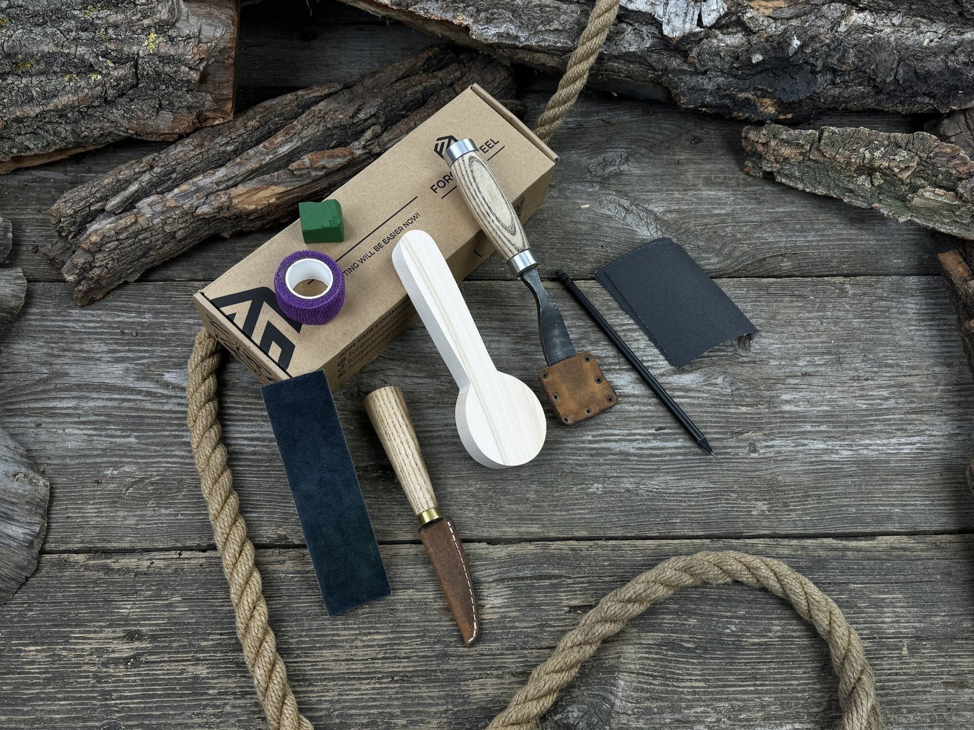 Spoon Carving Kit with knives, wooden blank, sandpaper, sharpening board, pencil, and finger wrap