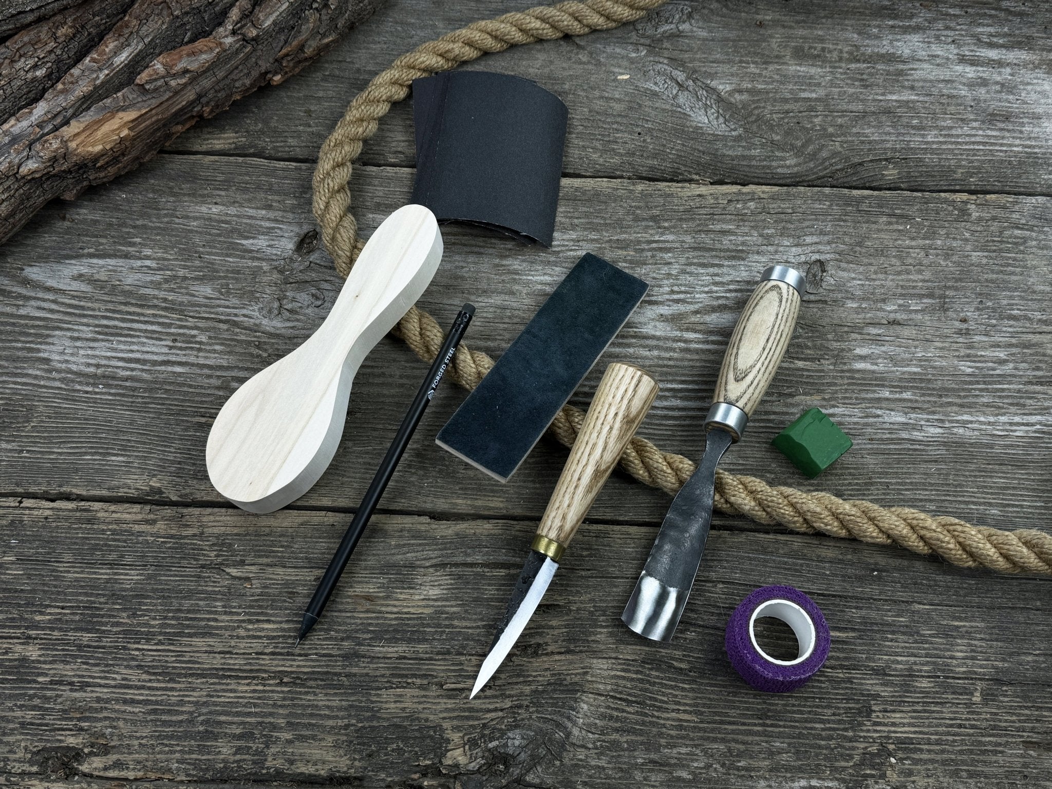 Spoon carving kit with sharpened tools, wooden blank, sandpaper, sharpening board, pencil, and finger wrap